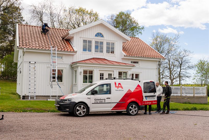 LA-bil på oppdrag ved hvit enebolig med takrens